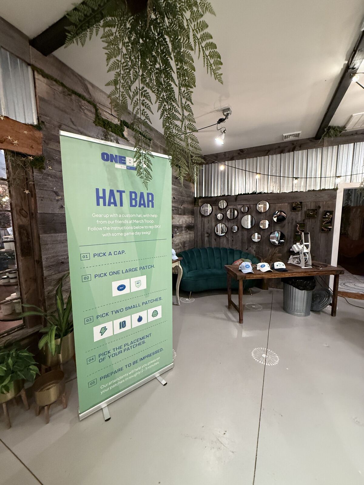 Styled customization lounge inside a rustic barn venue with velvet sofa, mirrors, and hanging greenery